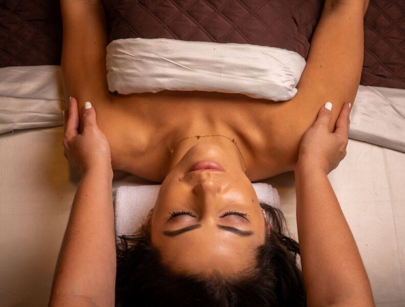 A persons arms are massaged while they lie on a massage table with their eyes closed.