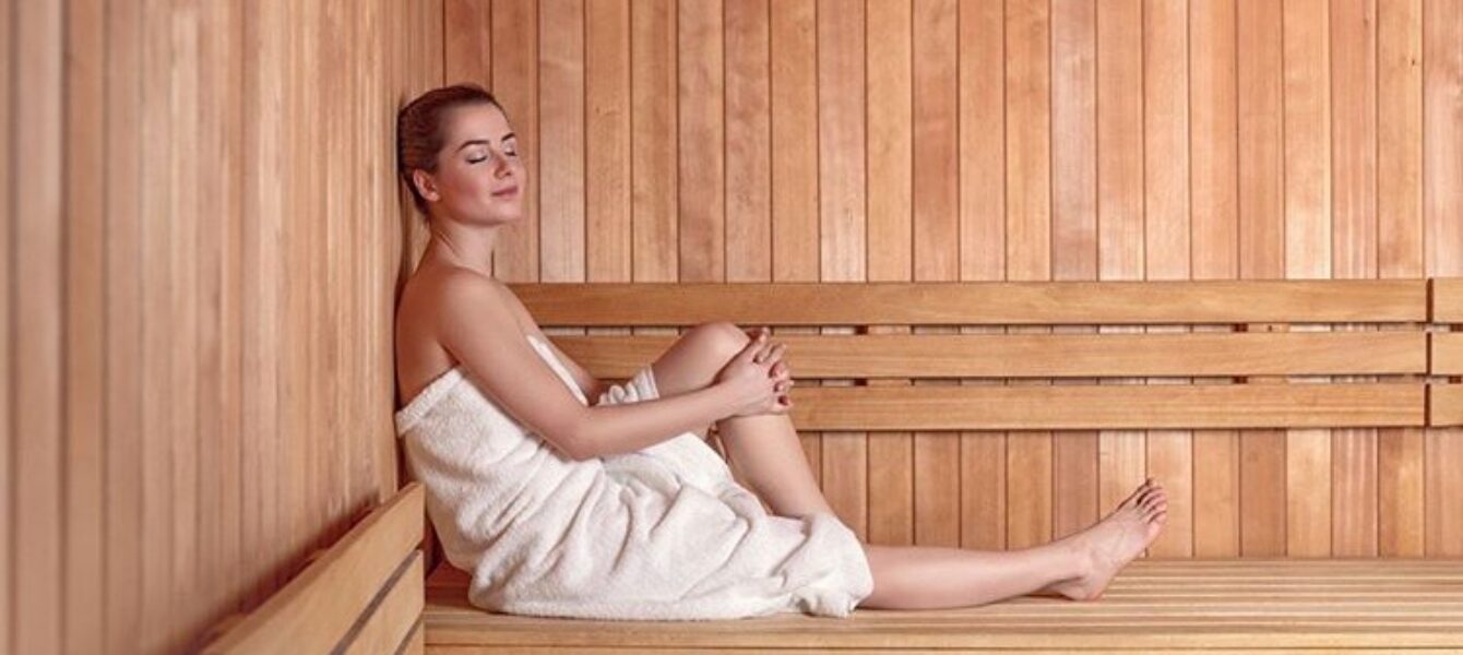 Woman relaxing in a wooden sauna, wrapped in a white towel.