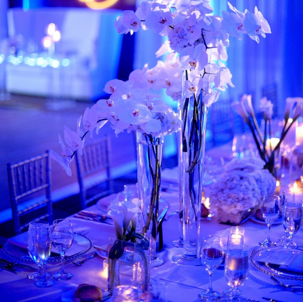 An elegant wedding reception setup with white orchids and blue lighting.