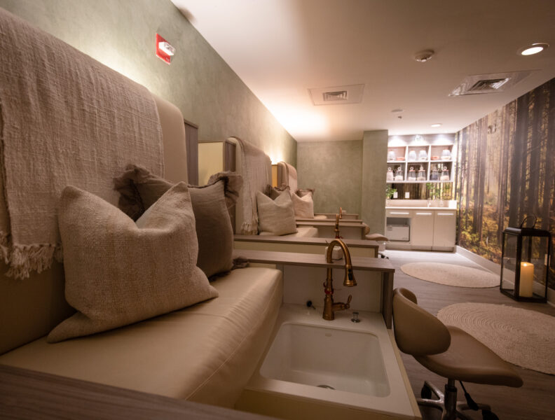 Pedicure spa chairs with plush pillows, foot basins, soft lighting, and a forest wall mural create a calm, relaxing atmosphere.